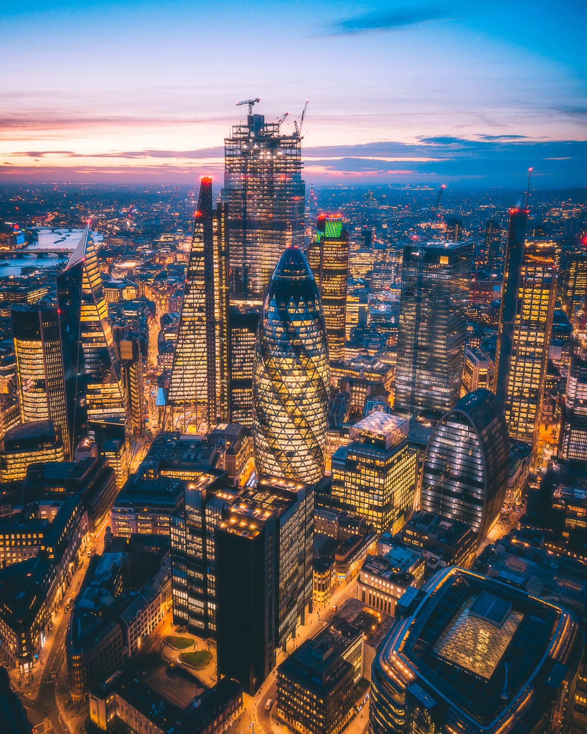 Aerial view of the City of London skyline at sunset, featuring iconic skyscrapers like the Gherkin and the Leadenhall Building.